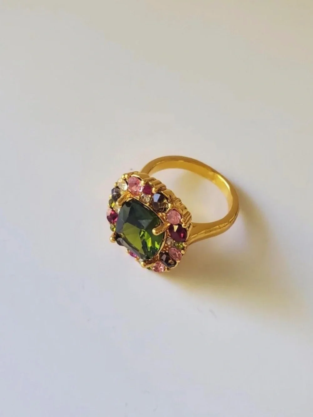 Gold ring with green central gemstone surrounded by pink and red rhinestones